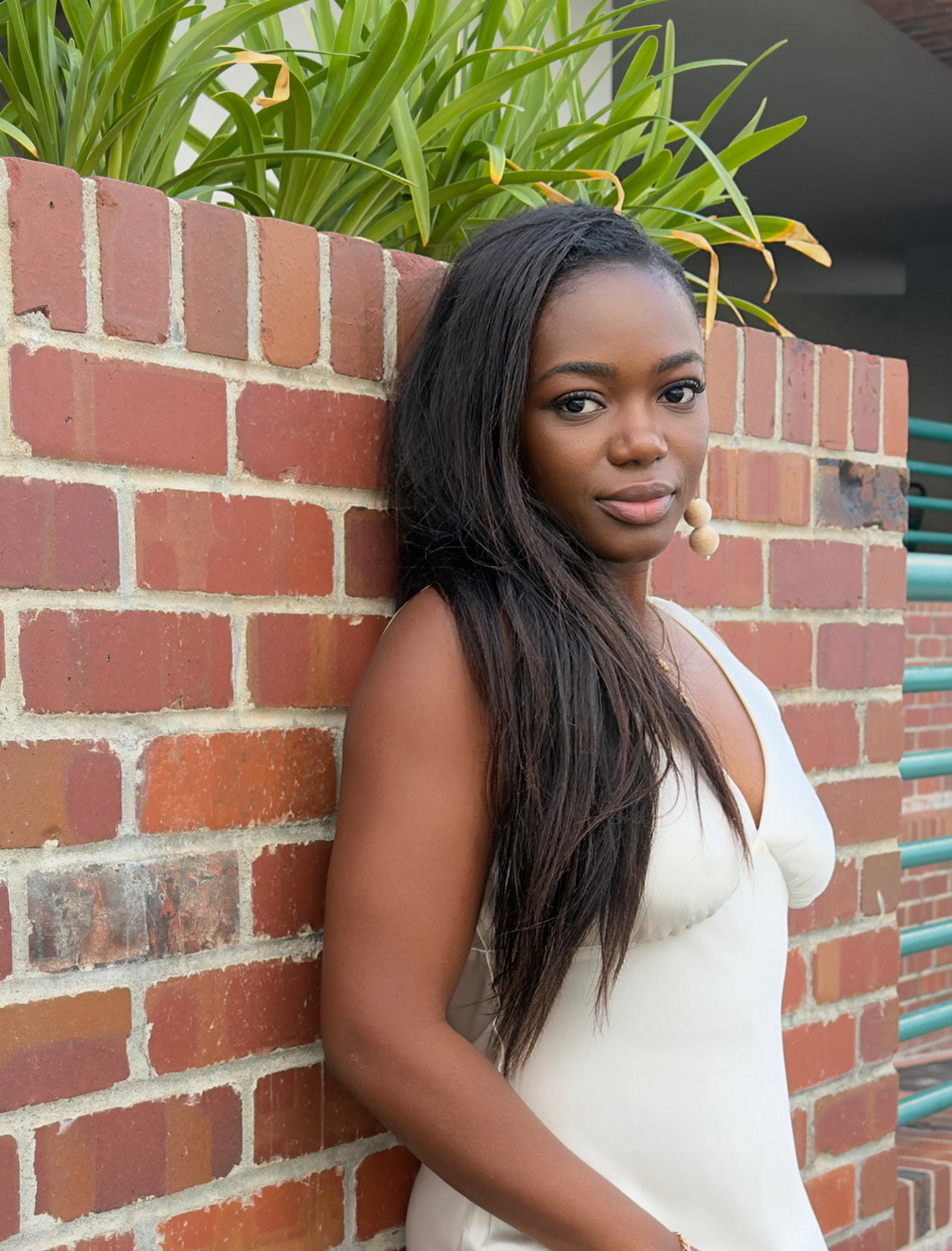 Julie Don in a cream slip dress leaning against a brick wall